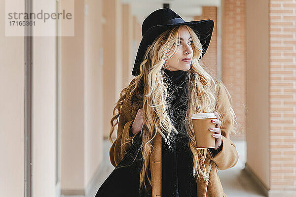 Woman in hat holding coffee cup while looking away