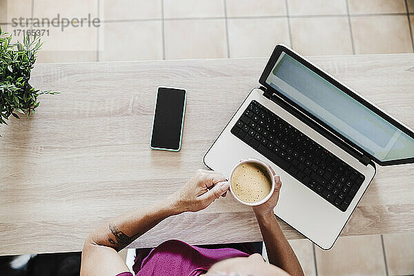 Geschäftsfrau mit Laptop und Kaffeetasse auf dem Tisch im Büro zu Hause