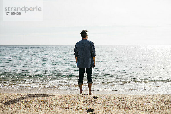 Mann steht an einem sonnigen Tag am Strand am Meer