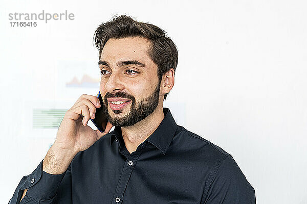 Young male entrepreneur talking on smart phone against wall