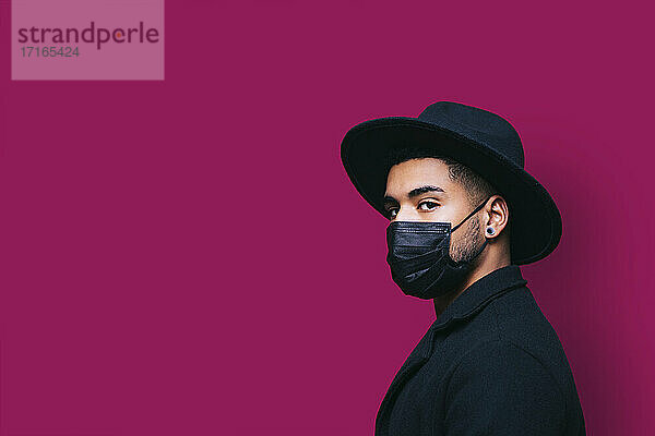 Man with protective face mask against pink background during pandemic