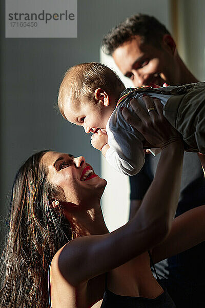Smiling woman playing with baby boy while standing by man at home