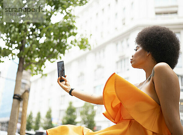 Young woman taking selfie through smart phone in city