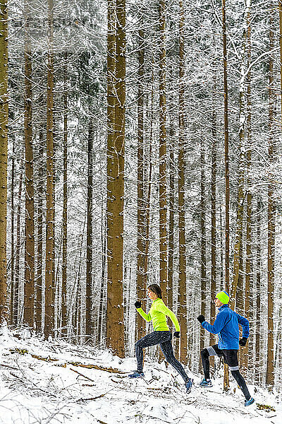 Male and female athletes running on trail in forest during winter