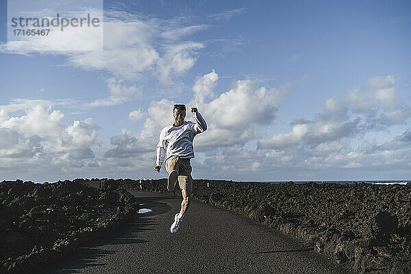 Fröhlicher männlicher Tourist  der an einem sonnigen Tag in Los Hervideros inmitten von Vulkangestein springt  Lanzarote  Spanien