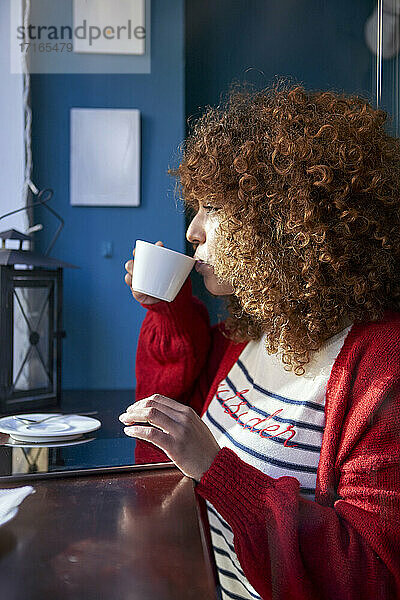 Curly hair woman drinking coffee while sitting at cafe