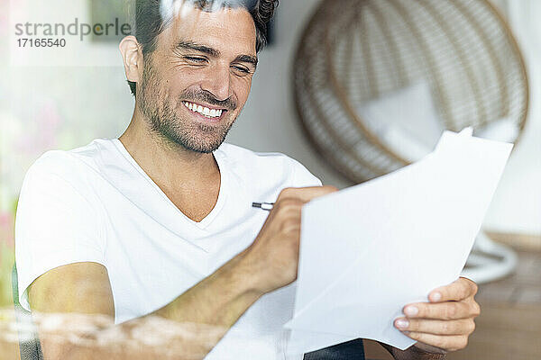 Lächelnder Mann  der bei der Arbeit zu Hause auf Papier schreibt