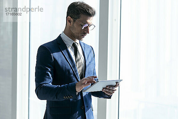 Geschäftsmann mit Brille  der ein digitales Tablet benutzt  während er im Büro steht