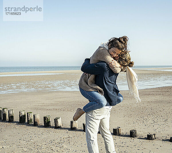 Junger Mann  der seine Freundin abholt und am Strand umarmt  an einem sonnigen Tag