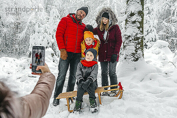 Frau fotografiert ihre Familie mit dem Handy  während sie im Winter im Wald steht