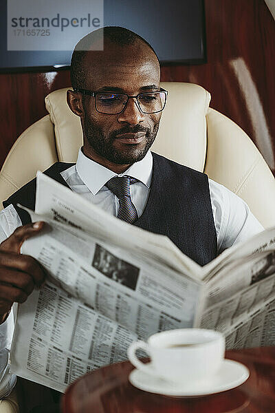 Männlicher Unternehmer liest Zeitung im Flugzeug