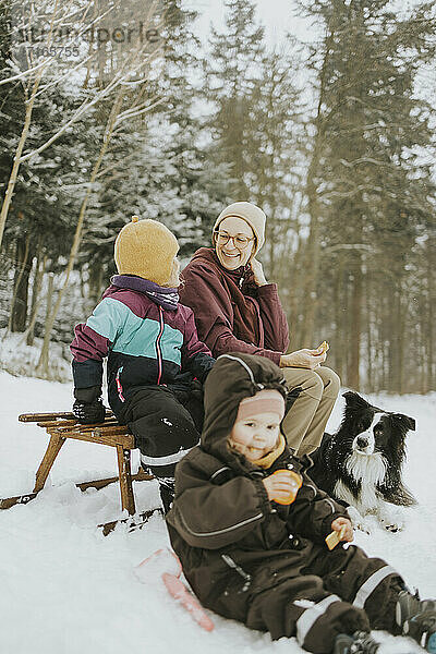 Familie mit Border Collie auf einem Schlitten sitzend auf einem verschneiten Feld am Wochenende