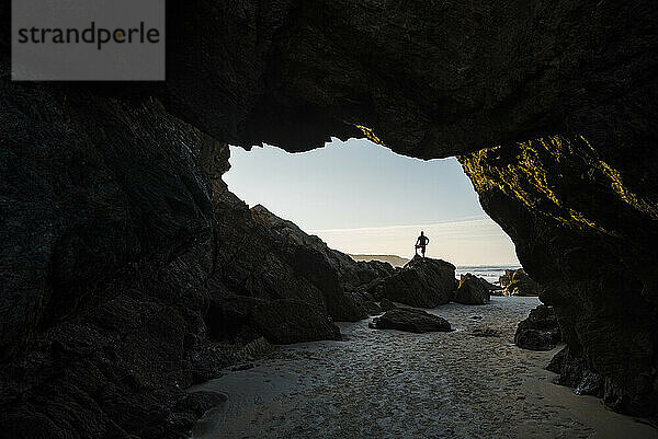 Silhouette eines Mannes  der auf einem Felsen am Eingang einer leeren Strandhöhle steht  Asturien  Spanien