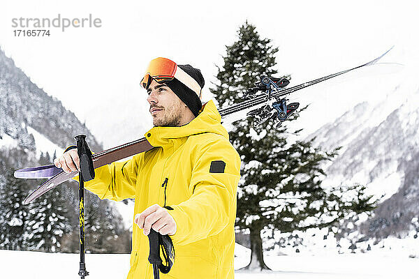 Thoughtful man with ski looking away while standing on snow covered valley