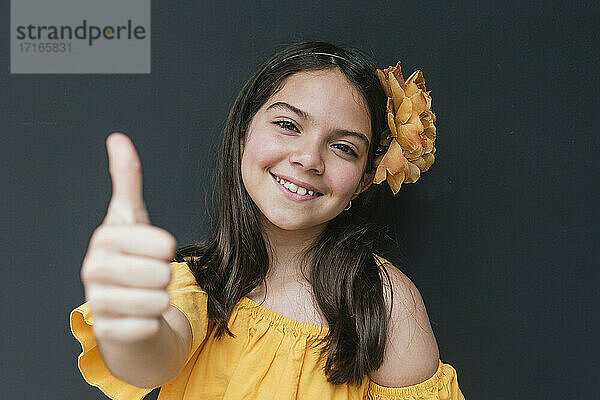Nahaufnahme eines lächelnden Mädchens mit gelbem Stirnband  das den Daumen nach oben zeigt  vor schwarzem Hintergrund