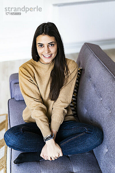 Young woman smiling while sitting cross-legged on sofa at home