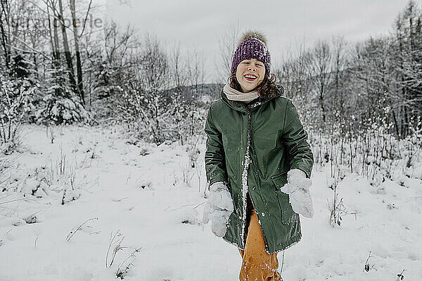 Lachendes jugendliches Mädchen  das Schnee hält  während es im Winter im Schnee steht