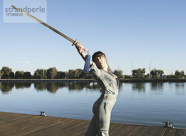 Junge Frau macht Kampfsport mit Schwert im Park am See an einem sonnigen Tag
