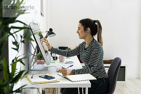Lächelnde junge Geschäftsfrau berührt den Bildschirm eines Computers am Arbeitsplatz