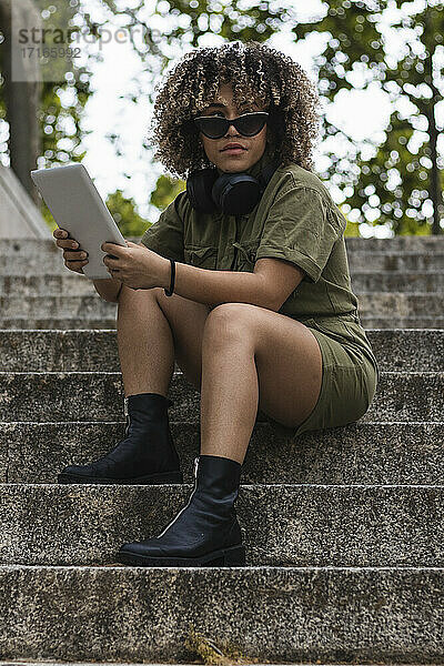 Frau mit digitalem Tablet sitzt auf einer Treppe vor Bäumen