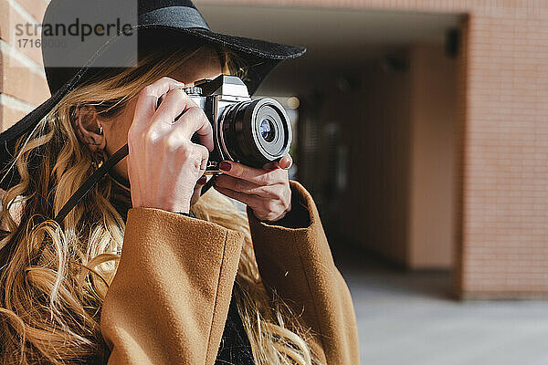 Young woman in hat filming through camera during sunny day