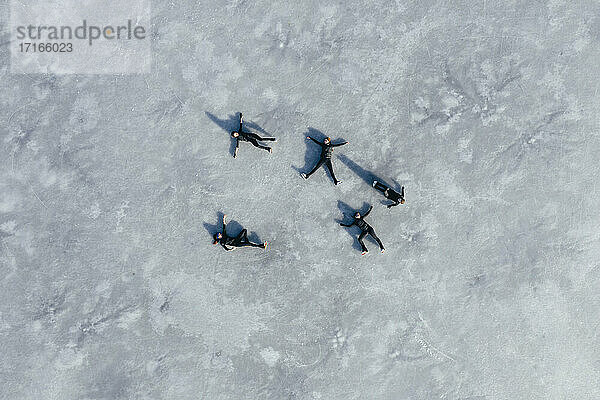 Aerial view of group of female ice-skaters lying together on surface of frozen lake