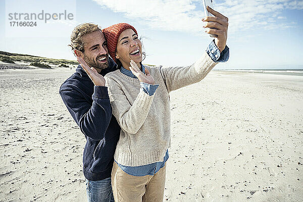 Porträt eines jungen Paares  das zusammen am Strand steht und ein Smartphone benutzt