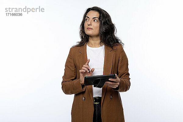 Nachdenkliche reife Frau mit digitalem Tablet  die vor weißem Hintergrund wegschaut