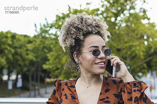 Lächelnde Frau  die wegschaut  während sie mit einem Handy in der Stadt telefoniert