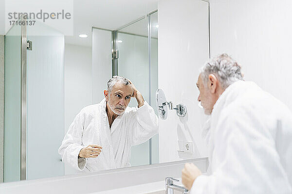 Handsome man looking at reflection in mirror of hotel bathroom