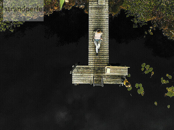 Luftaufnahme einer reifen Frau  die auf einem Steg über einem See im Wald sitzt