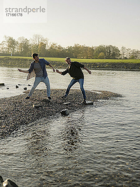 Father and son throwing pebbles in river during autumn