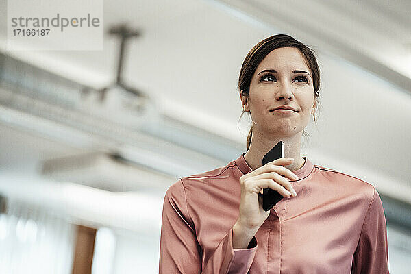 Unternehmerin beim Nachdenken über ihr Smartphone im Büro