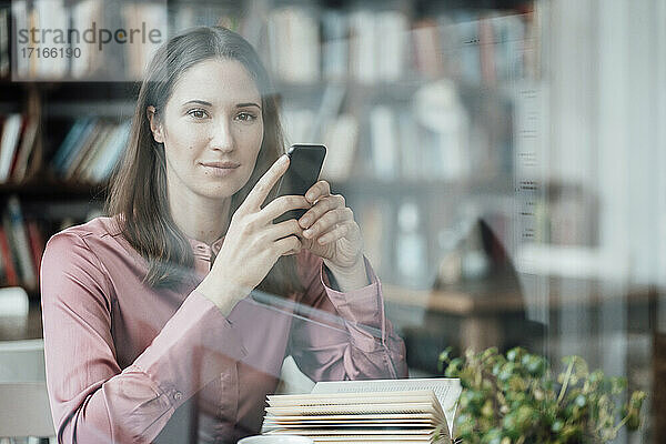 Unternehmerin mit Buch und Handy in der Hand schaut durch ein Glas in einem Cafe