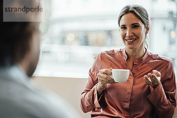 Eine lächelnde Geschäftsfrau trinkt Kaffee und diskutiert mit einem männlichen Kollegen in einem Café