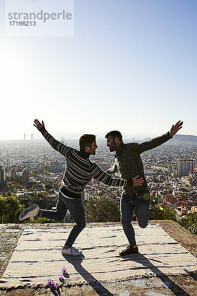 Fröhliches schwules Paar mit ausgestreckten Armen tanzt auf einem Aussichtspunkt  Bunkers del Carmel  Barcelona  Spanien