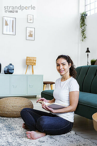 Smiling woman reading book while sitting at home