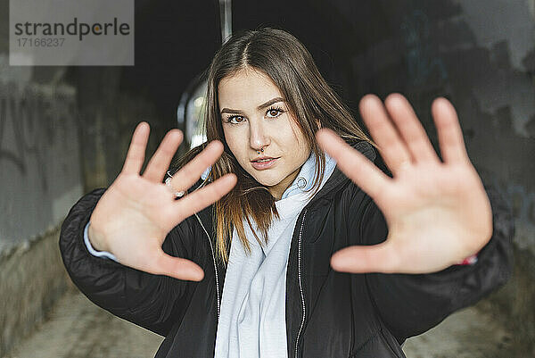 Young woman wearing jacket stretching hand while standing against underpass