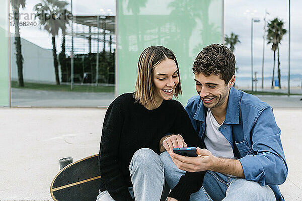 Lächelndes Paar  das im Freien auf sein Smartphone schaut