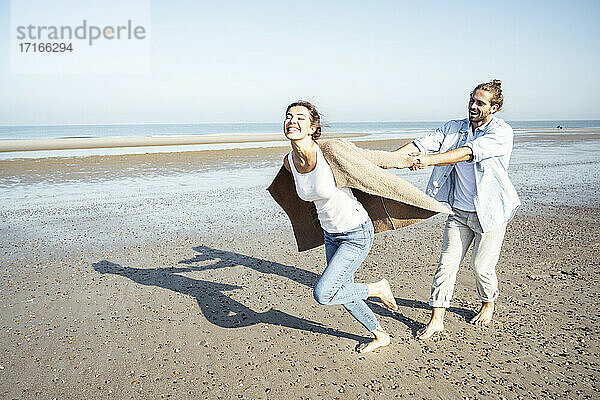 Junger Mann hält die Hände seiner Freundin  während er am Strand im Sand läuft