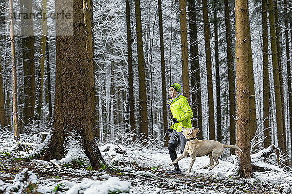 Junger Sportler läuft mit seinem Hund im Winter im Wald
