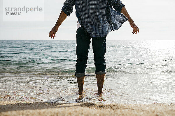 Älterer Mann steht am Rande des Wassers gegen den klaren Himmel am Strand
