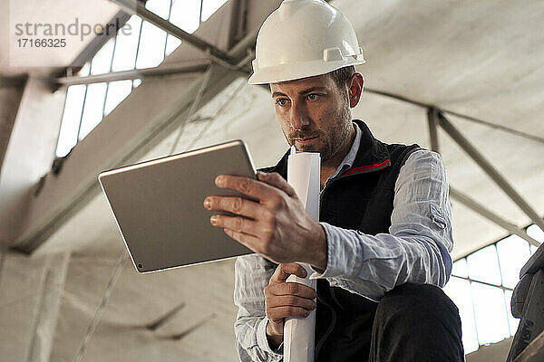 Seriöser männlicher Ingenieur  der ein digitales Tablet benutzt  während er in einem Gebäude auf der Baustelle steht