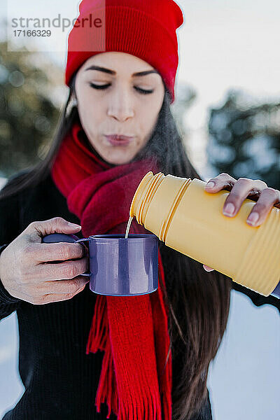 Nahaufnahme einer Frau  die Kaffee in eine Tasse gießt  während sie im Winter im Freien steht