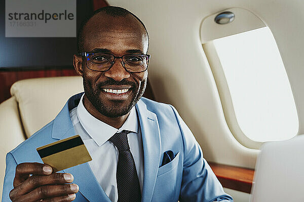Lächelnder männlicher Unternehmer mit Kreditkarte im Flugzeug