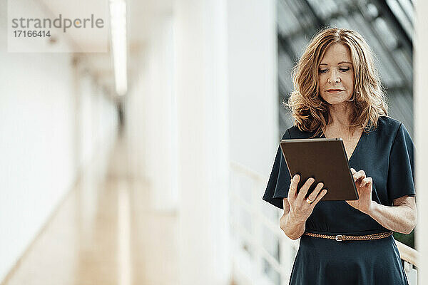Ältere Geschäftsfrau  die ein digitales Tablet benutzt  während sie im Korridor steht