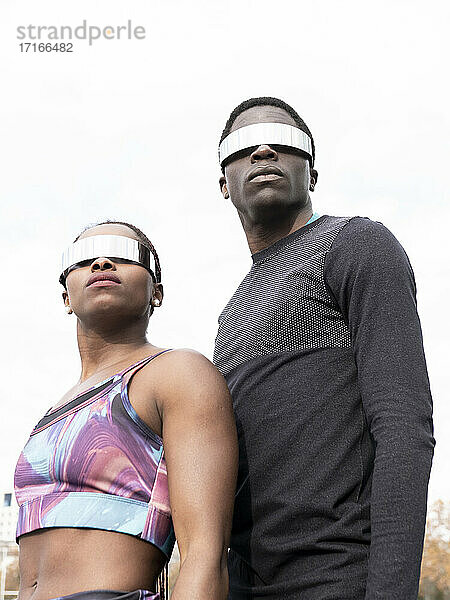 Sportler und Sportlerin mit Sonnenbrille schauen gegen den klaren Himmel weg