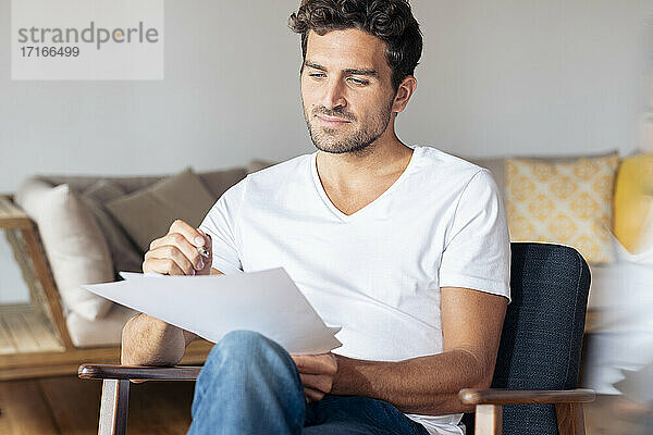 Mann konzentriert sich auf Papier  während er zu Hause auf einem Sessel sitzt