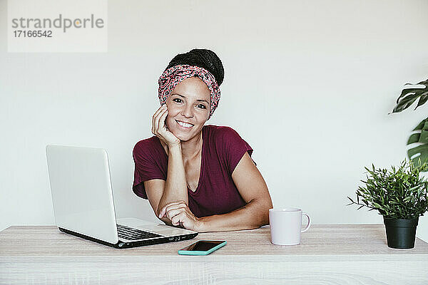 Geschäftsfrau am Laptop lächelnd mit Hand am Kinn zu Hause