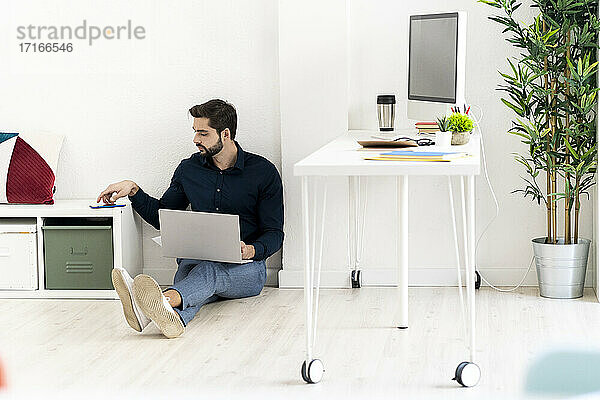 Male entrepreneur with laptop and smart phone while sitting against white wall in office